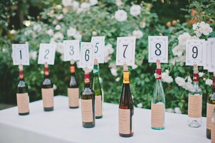bouteilles de vin personnalisés avec étiquettes invités collées dessus et nombre de table dans une fente du bouchon de liège, diy mariage plan de table