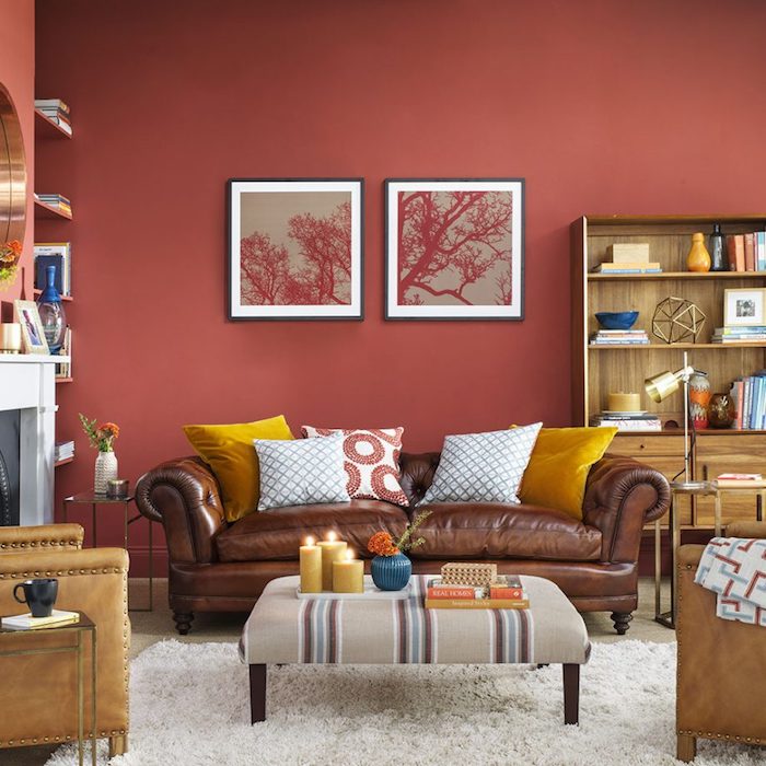 peinture rouge sur le mur dans un salon, moderne aux accents jaunes, canapé et fauteuils en cuir avec des coussins jaunes et blancs, tapis blanc, bibliothèque en bois, deco romantique, cheminée