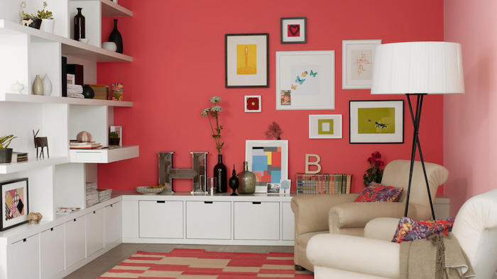 peinture rouge tirant vers le rose saumon dans un salon moderne avec riche deco murale de cadres et accessoires deco, bibliothèque et meubles de rangement blancs