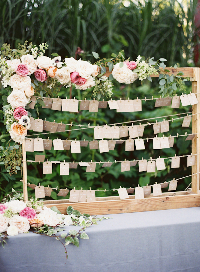 plan de table mariahe en cadre en bois avec des étiquettes en papier kraft avec des noms invités pour trouver sa place, guirlande de fleurs fraîches