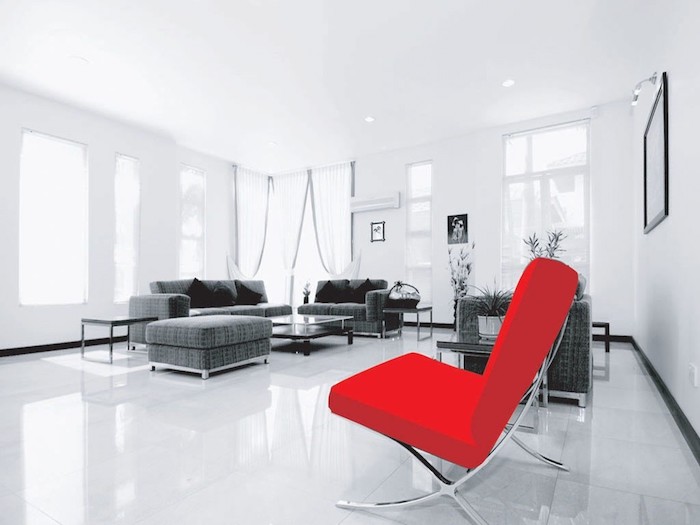 modele de salon moderne, quelle couleur associer au gris, murs, sol et plafond blancs, canapé et tabouret gris, coussins décoratifs noirs, fauteuil rouge vermillon