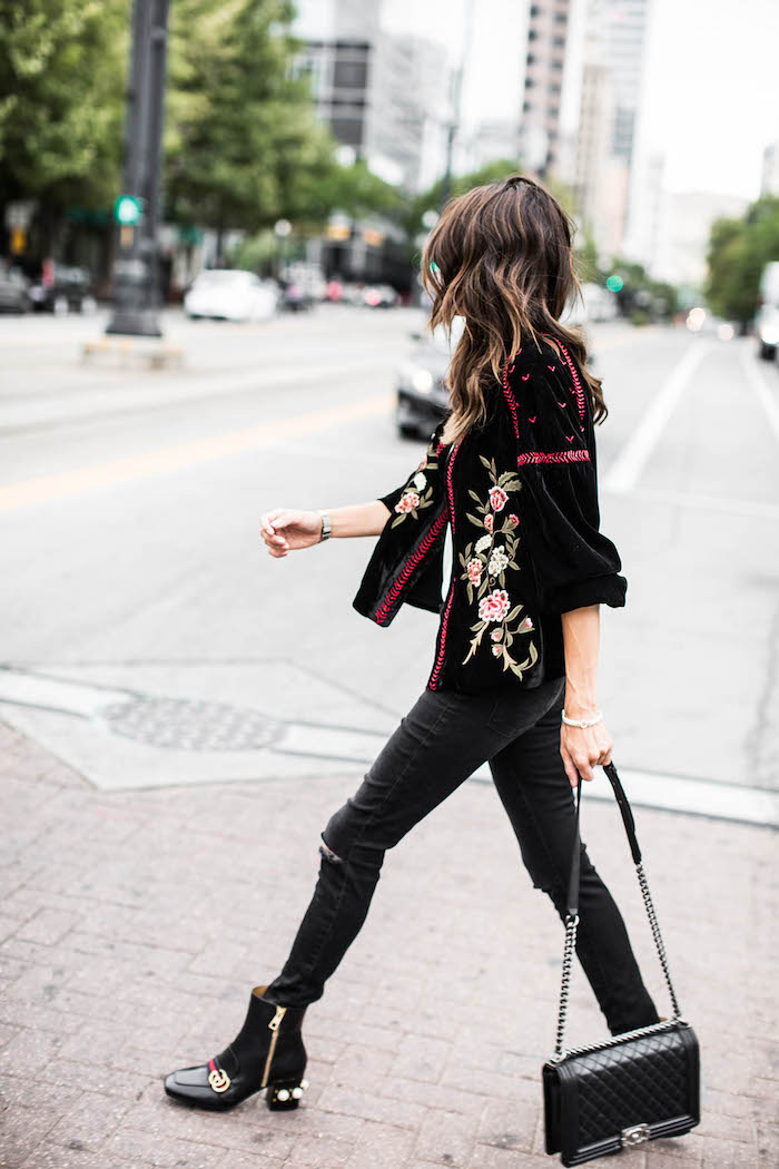 tendance fashion, veste noire avec broderie à motifs floraux rose et vert, pochette en cuir noir avec poignée métallique