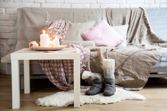 salon cocooning, avec canapé gris, couverture marron clair et rose, coussins decoratifs marron et rose, table basse blanche, tapis fausse fourrure, bougies romantiques