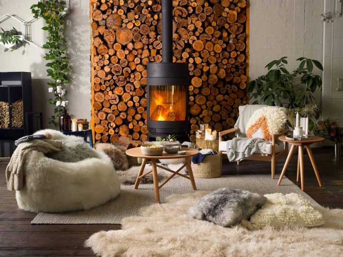 idée de salon cocooning chaleureux, cheminée moderne avec un fond de bûches de bois, tapis et fourrure beige, fauteuil blanc de peau animale, chaise et table en bois, parquet marron