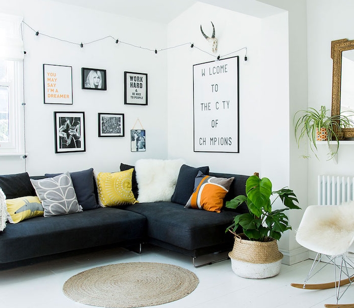 salon cocooning blanc avec canapé noir, revêtement sol blanc, tapis rond, chaise scandinave avec jeté de fourrure, coussins decoratifs colorés, mur de photos en noir et blanc