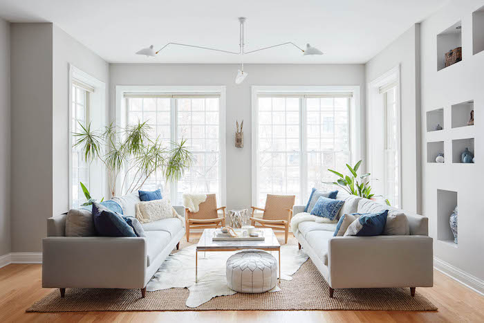 tapis cocooning dans un salon avec canapés gris, table basse, pouf blanc, chaises beiges, palmier, mur avec rangements intégrés