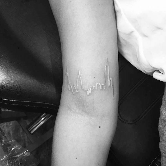 photo blanc et noir, tatouage blanc sur le bras à design lumières de la ville, tattoo pour femme