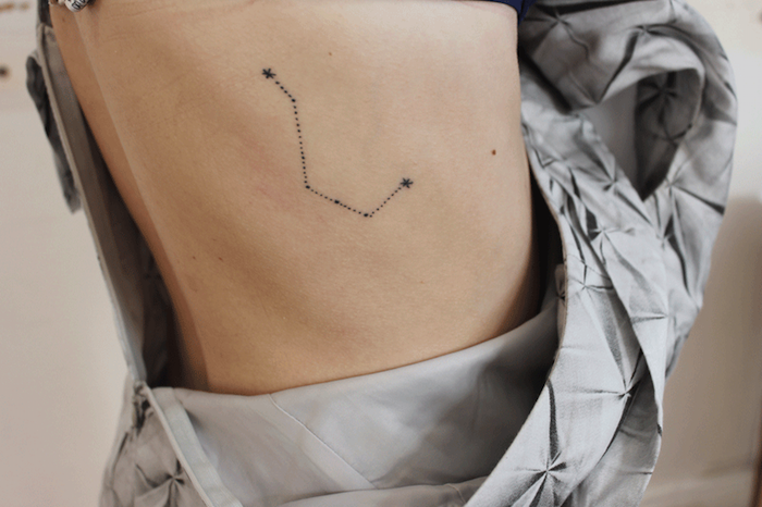 tatouage dos femme, robe grise à motifs ruban, dessin en encre à design constellation d'étoiles