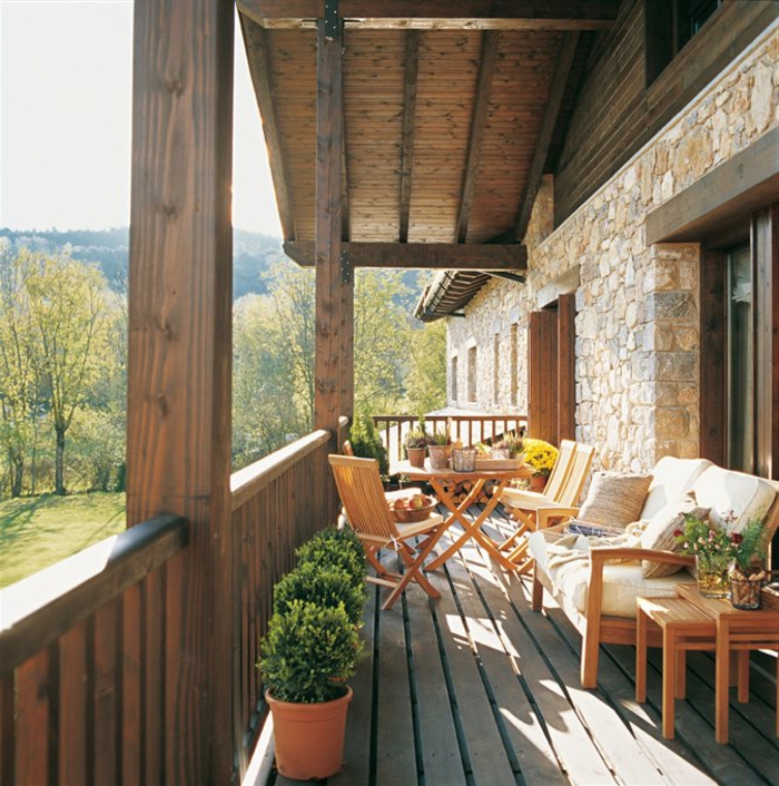 aménager une terrasse en bois, table et chaises, canapé en bois, plantes dans des pots de fleurs, boules buis, mur en pierre