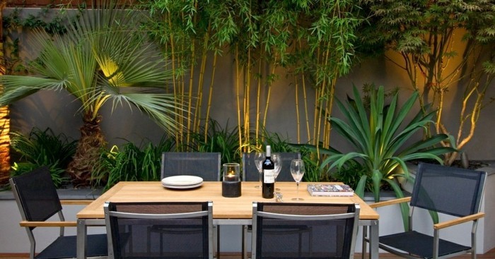 amenagement terrasse zen avec coin salle à manger en plein air, table bois, chaises noires, bambou et arbustes verts