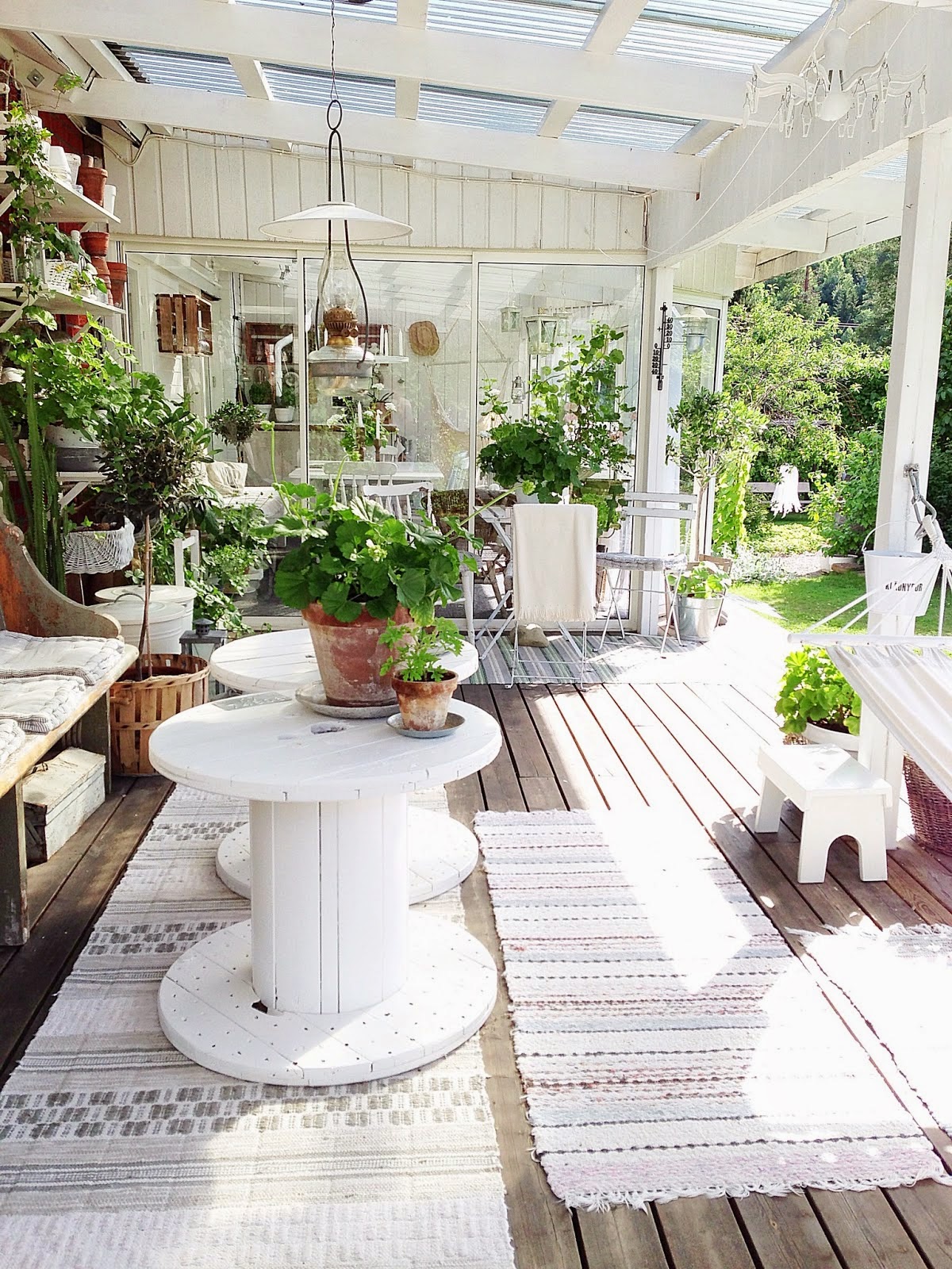 idée de décoration terrasse exterieur avec banc en bois brut et tables en touret blancs, touret bois deco avec beaucoup de plantes vertes