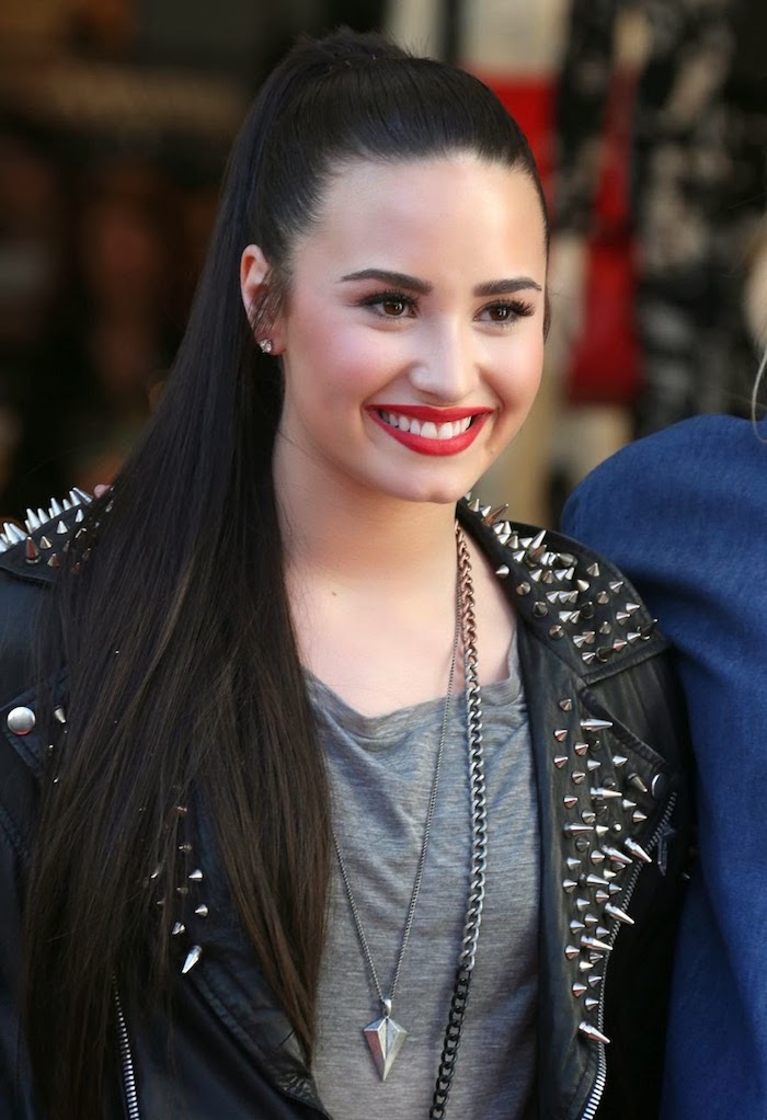 coiffure célébrité cheveux longs et noirs Demi Lovato, style rock femme avec veste en simili cuir noir avec studs
