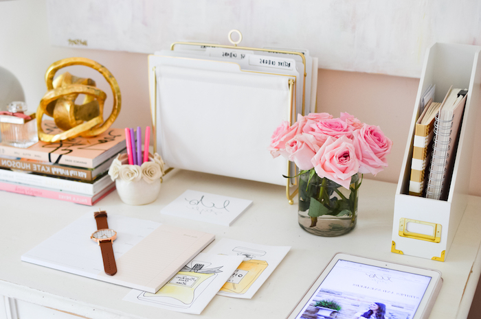 bureau avec plan de travail, classeur de magazines blanc et or, collections de livre fashion, petite vase blanche à deco avec roses