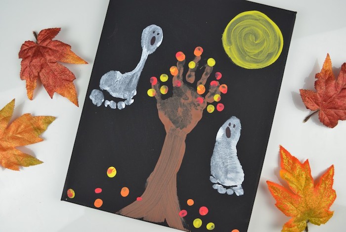 dessin sur une pancarte noire avec arbre empreinte de main et des fantômes empreintes de pieds, lune, feuilles mortes
