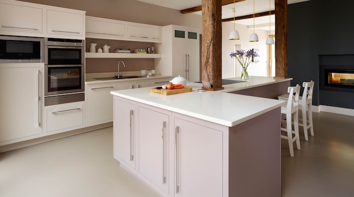 ilot central cuisine d'angle avec comptoir blanc et armoires rose pastel, cheminée moderne et noire dans la cuisine