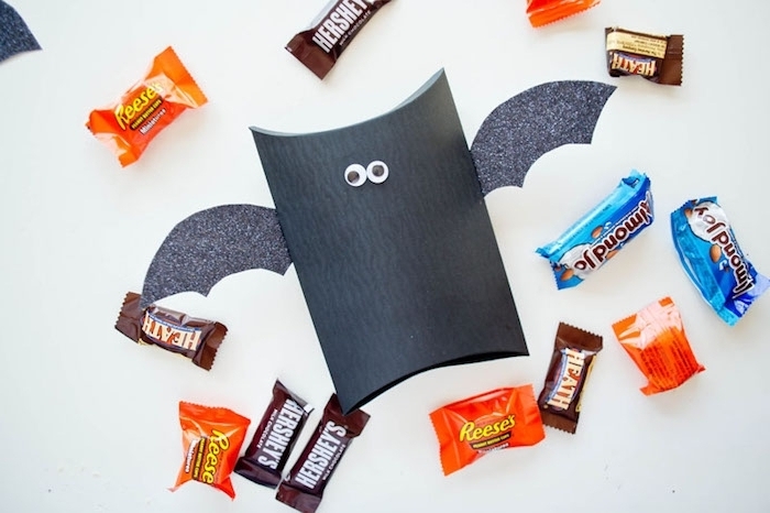 bricolage halloween avec rouleau de papier toilette, repeint en noir, des ailes en papier gris et des yeux mobiles, bonbons colorés