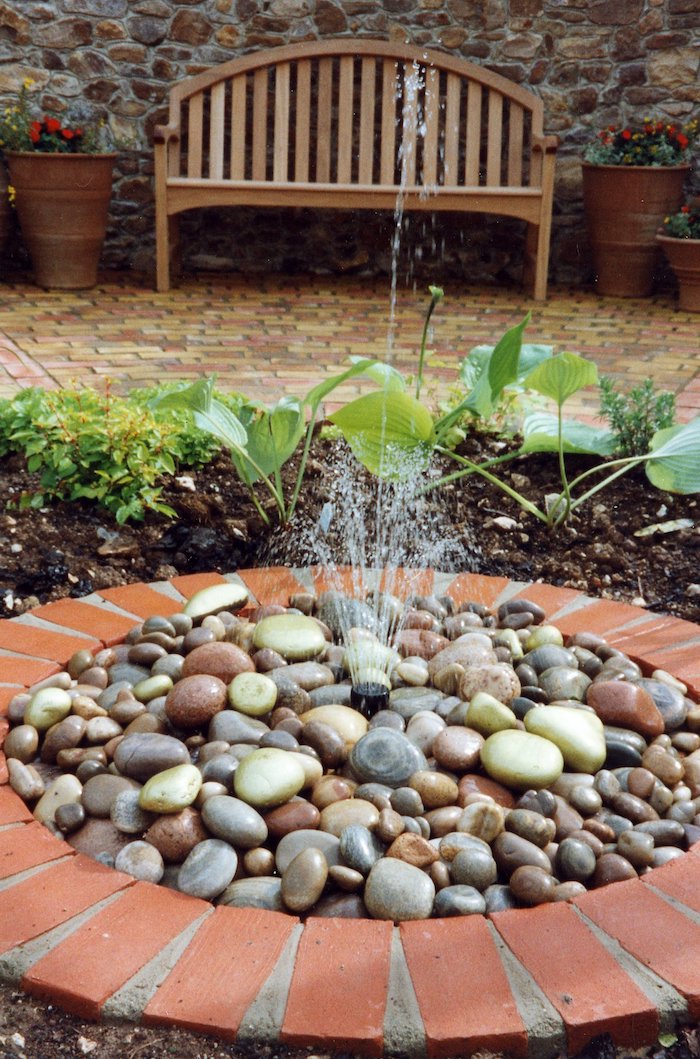 idee deco jardin, créer une petite fontaine dans le jardin avec cailloux et pierres, banc de jardin en bois