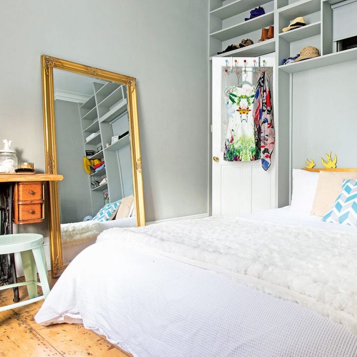 chambre gris et blanc, avec grand miroir couleur cadre doré, linge de lit blanc, etageres mursles, parquet bois brut