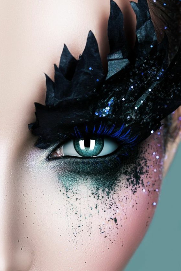 maquillage yeux bleu de style excentrique en vert bleu électrique et noir avec des sourcils bleu flashy se terminant avec des décorations en forme de plumes noires d'oiseau