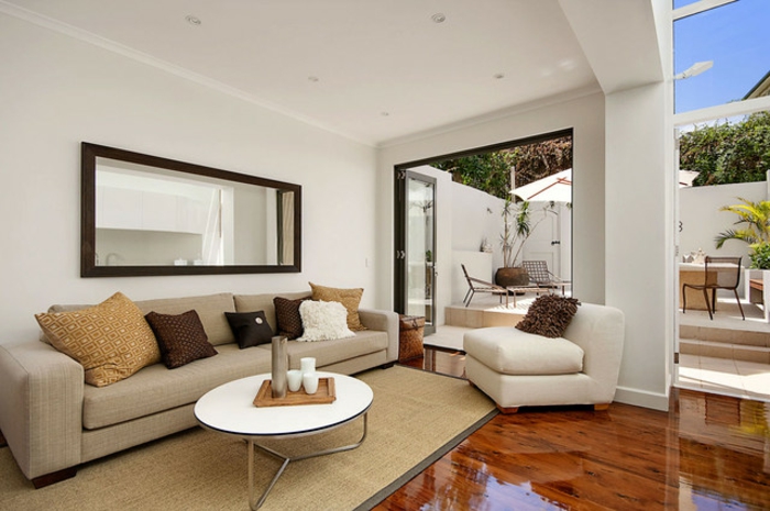 cosy deco, table blanche ronde, sofa beige avec plusieurs coussins, fauteuil blanc, sol en bois, peinture murale blanche