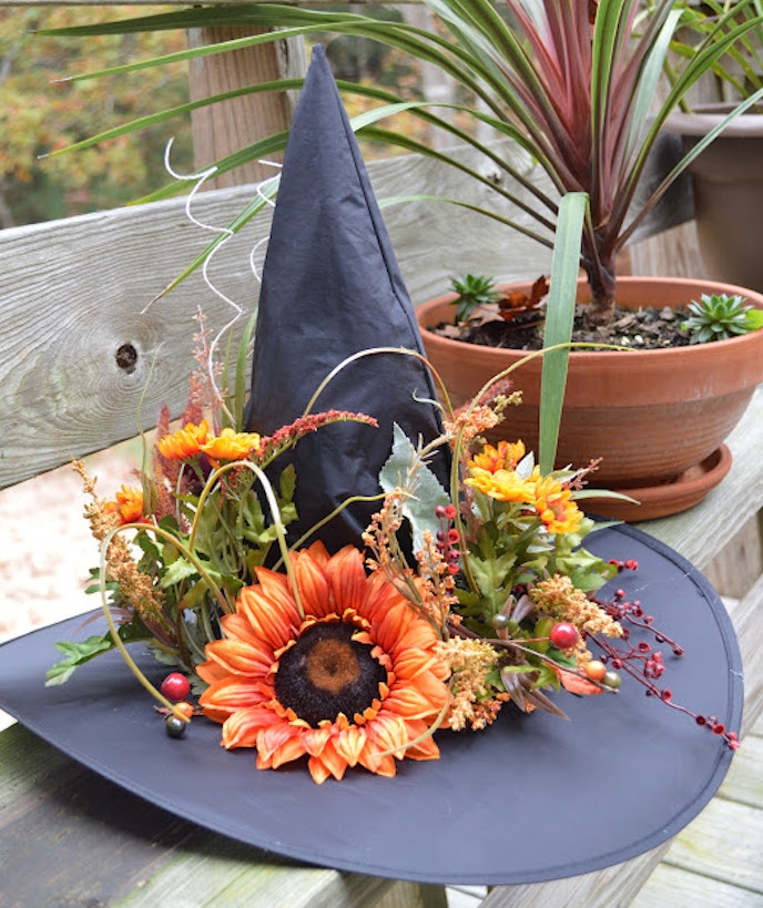 un chapeau de sorcière noir avec decoration de fleurs, sur un banc en bois, deco halloween a faire soi meme