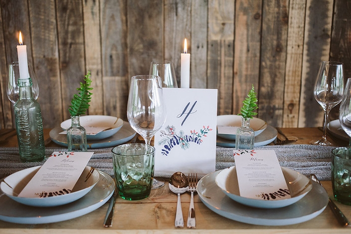 idée déco mariage simple rustique, table en bois brut, bouteilles en verre avec des bougies, fioles avec des brins de feuilles, chemin de table gris