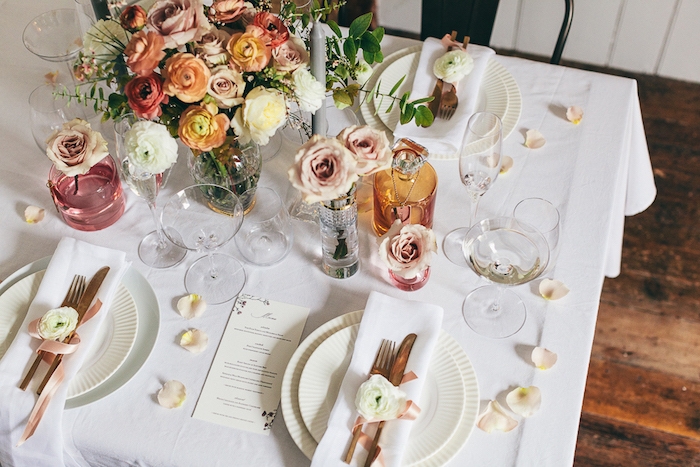 deco mariage pas cher, fleurs arrangées dans des talles, bouteilles et bocaux colorés et pétales de roses dispersées sur al table, serviette blanche et couverts décorés de fleur et ruban rose