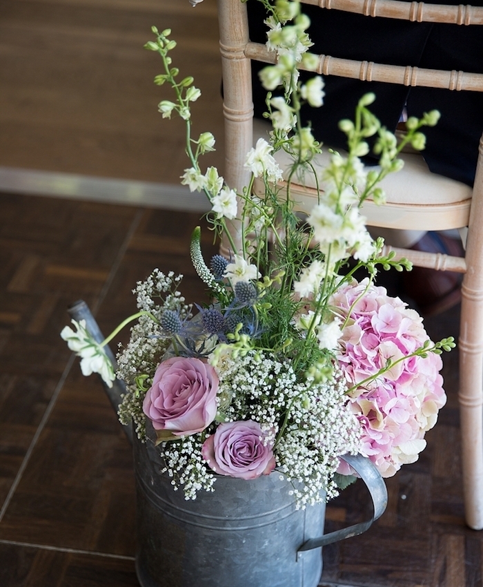 idee de deco mariage champetre, arrosoir vintage en zinc avec bouquet de fleurs dedans, derrière une chaise