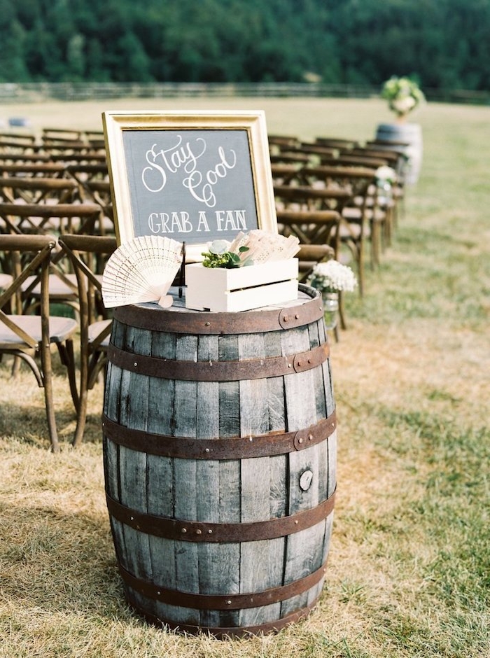 exemple de deco mariage champetre chic, tonneau en bois et metal avec un cagette en bois remplie d éventails pour les invités