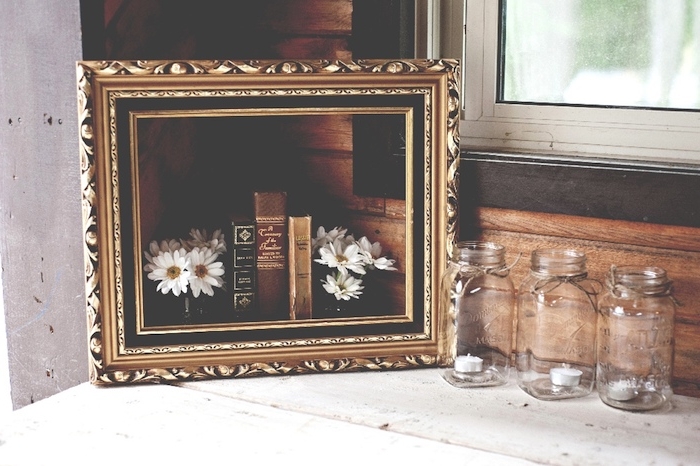 exemple de deco mariage vintage avec cadre peinture vintage, bouquins retro, bougeoirs en pots en verre avec des bougies, petits bouquets de marguerittes