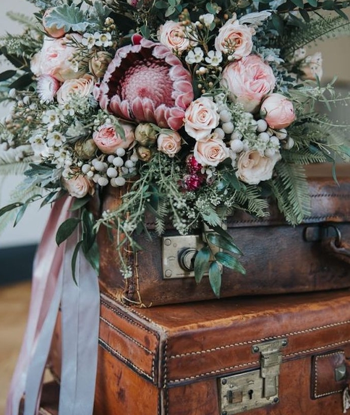 une pile de malles vintage en cuir aec un bouquet de fleurs en dessus et ruban rose, deco mariage vintage