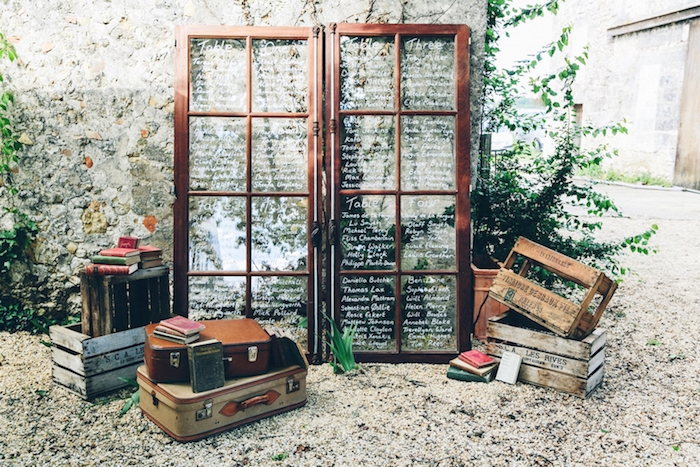 deco mariage vintage rustique avec des portes en bois et verre et listes invités écrits sur les carreaux, malles vintage et cagettes en bois, plantes vertes