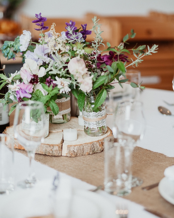 decoration table mariage avec chemin de table en toile de jute, rondelle en bois avec des pots en verre avec des bouquets de fleurs et déco en dentelle, jute et ficelle