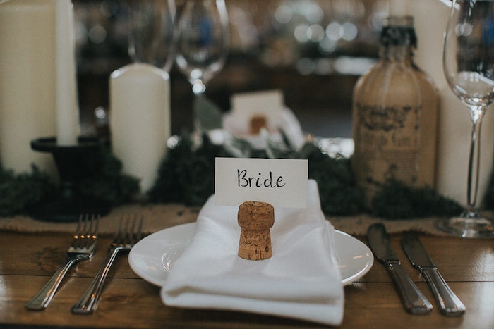decoration table mariage, serviette blanche, bouchon de liège avec carton nom invité, table en bois rustique, bougies, bouteille, guirlande deco