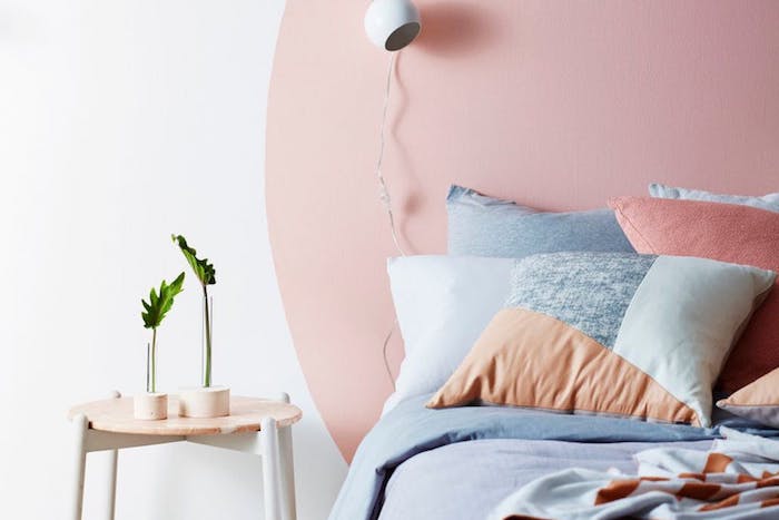 modele déco chambre cocooning, peinture murale blanche avec un cercle rose en guise de tete de lit, linge de lit rose, gris, saumon, table de nuit scandinave