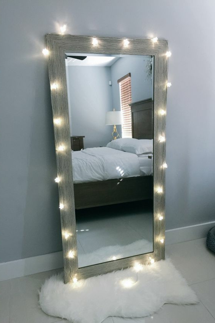 deco chambre adulte avec grand miroir entouré d' une guirlande aux ampoules lumineuses et posé sur un petit tapis blac en fausse fourrure