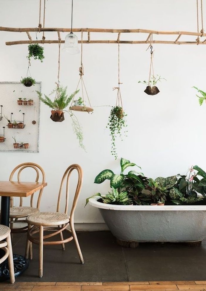 echelle en bois suspendue du plafond, rangements de pots de fleurs suspendus, baignoire grise avec des plantes vertes dedans, table et chaises en bois