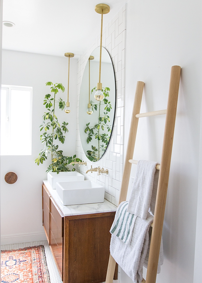 echelle porte serviette en bois clair dans la salle de bain, miroir rond, meuble sous vasque bois, plante verte, tapis oriental