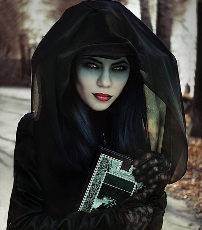exemple de déguisment femme halloween sorcière, peau teinte verte, chapeau, robe et cape noirs, grimoir, rouge a lèvres foncé