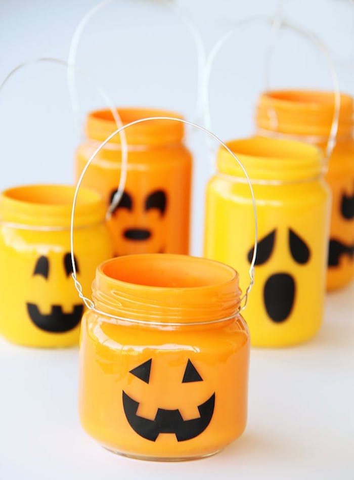bricolage halloween avec des pots en verre, repeints de peinture orange à l interieur et des traits de visage noirs jack o lantern a l exterieur