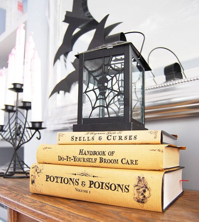 activite halloween, une lanterne noire avec des livres sorcellerie entassés, bougeoir noir et des silhouettes chauve souris en papier