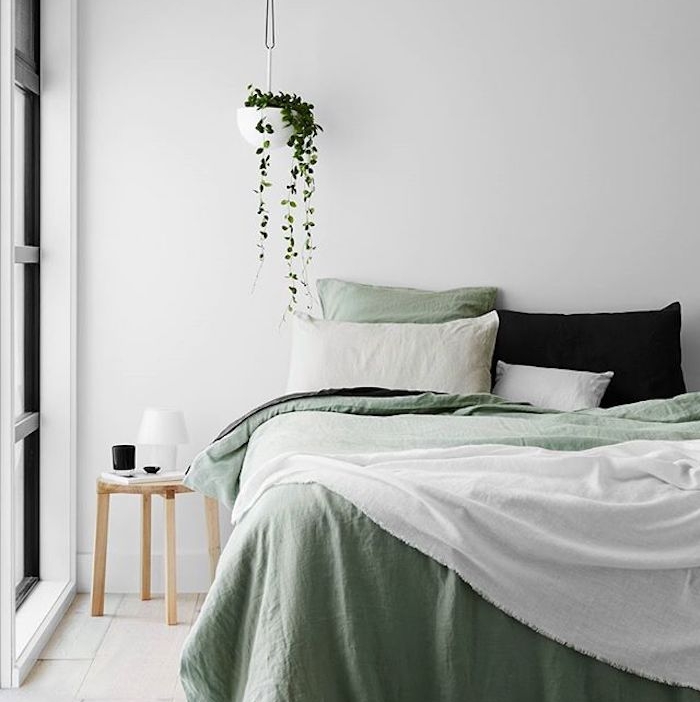 décoration chambre adulte, mur couleur blanche, linge de lit blanc et vert, coussin noir, parquet clair, table de nuit bois, plante verte suspendue