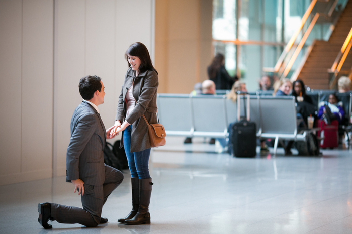 demande de fiancaille à l aéroport dans la salle d attente, femme surprise et homme sur ses jambes