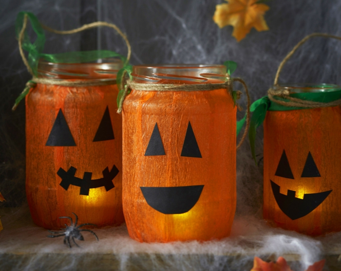 activite halloween avec des pots en verre, customisés de papier crepon collé dessus et des traits de visage noires, bouche et des yeux