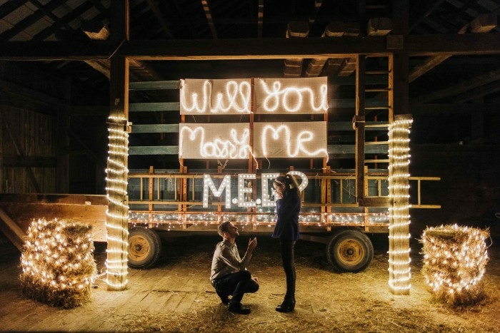 des lettres illuminées, guirlandes lumineuse, lettres neon pour faire une demande en mariage romantique dans un hangar