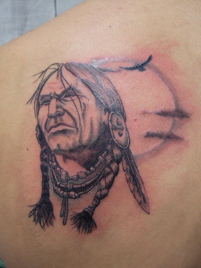 tatouage pour homme sur le dos, dessin en encre avec visage homme autochtone et plumes dans les cheveux