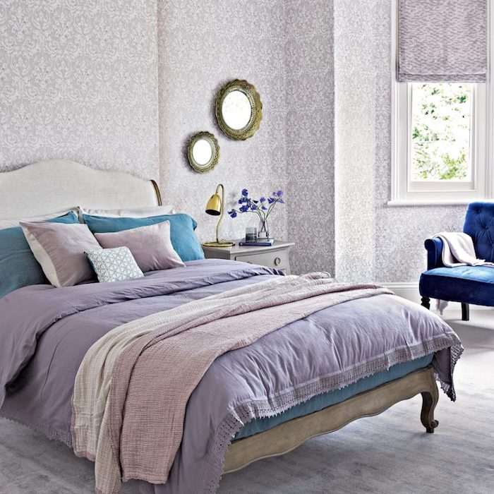 papier peint chambre adulte, motifs floraux gris sur un fond blanc, lit bois vintage, linge de lit violet, bleu et rose, fauteuil bleu marine