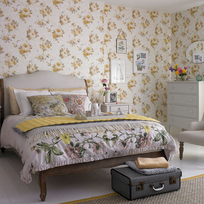 modele de papier peint vintage à imprimé floral, fleurs jaunes sur un fond blanc, lit bois, parquet clair, malle vintage gris en guise de bout de lit, coussins, couverture imprimé floral