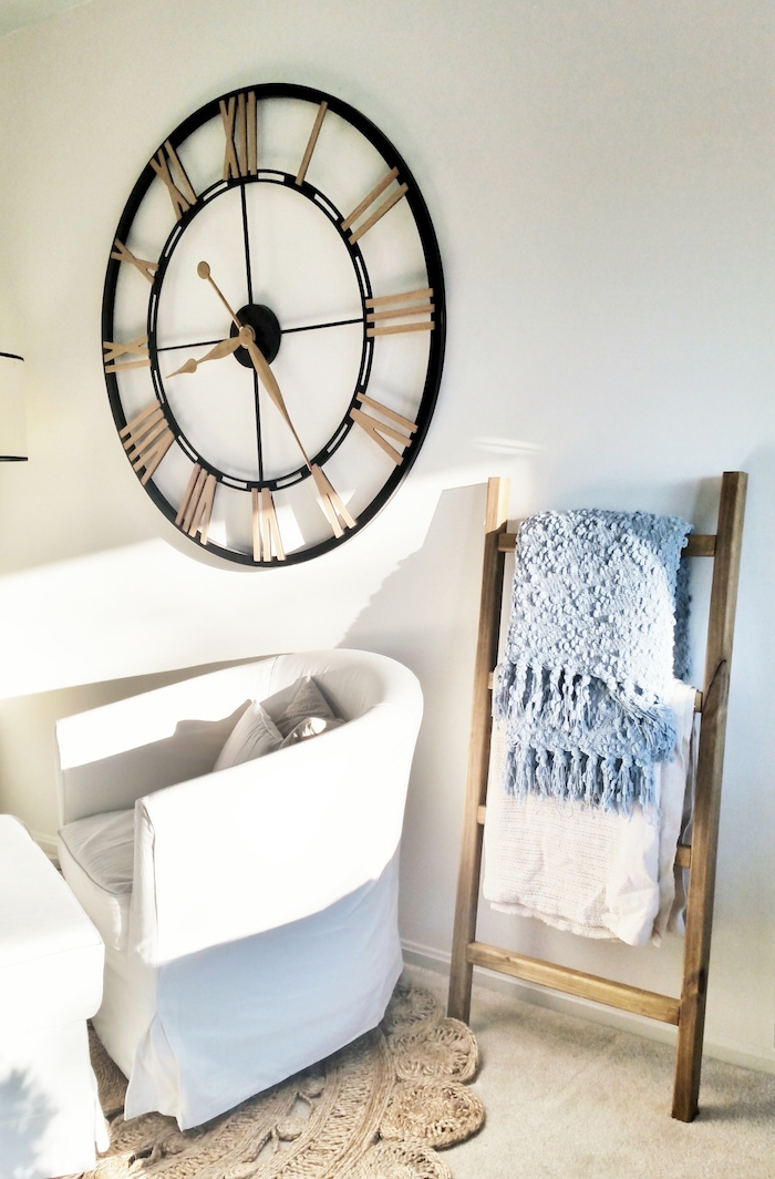 petite echelle en bois brut, rangement textiles, couvertures dans un salon scandinave, horloge vintage, canapé et table blancs