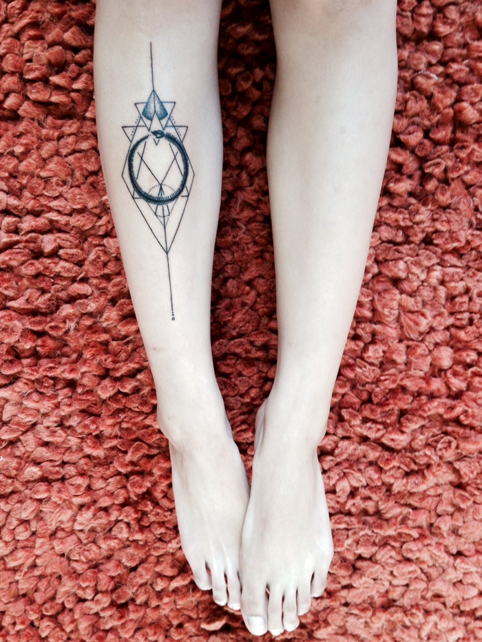 un tatouage vertical symbolique avec une forme géométrique et un ouroboros à l intérieur réalisé sur la jambe
